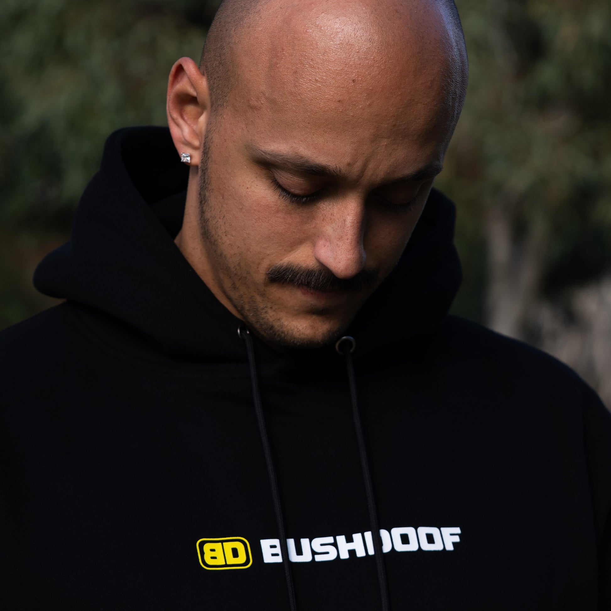 Bushdoof Staple Hoodie in black, worn outdoors
