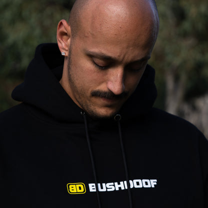 Bushdoof Staple Hoodie in black, worn outdoors