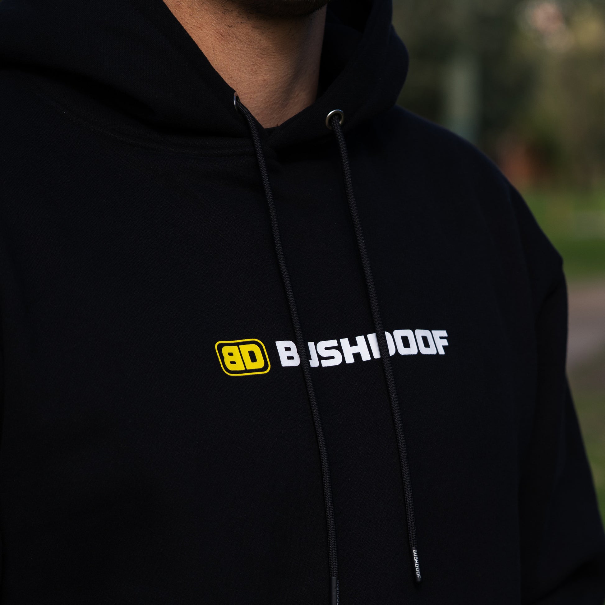 Bushdoof Staple Hoodie in black, worn outdoors